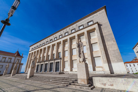 A modern building with large letters on the facade stands on a patterned stone plaza, featuring statues and a clear blue sky in the background.の写真素材
