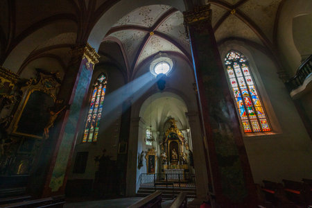 Interior view of a church featuring a striking beam of light piercing through the arched architecture, highlighting stained glass windows and ornate details.の写真素材