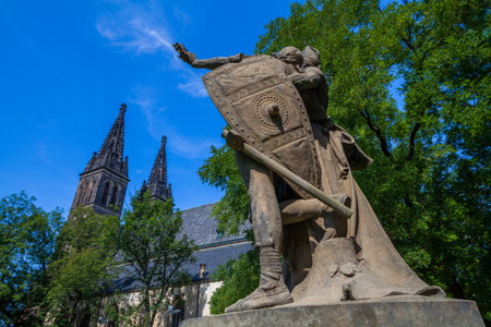 A large church with twin towers and a steeply pitched roof, featuring arched windows and decorative elements, sits behind a low wall and green space under a bright blue sky.の写真素材