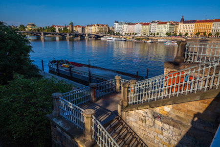 A cityscape featuring a river with multiple bridges, boats moored along the banks, ornate buildings lining the waterfront, and a staircase leading down to the riverbank in the foreground.の写真素材