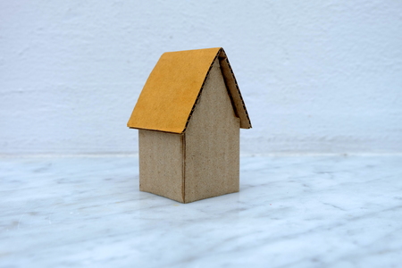 Cardboard House on Marble Floor with White Concrete Wall Background.の写真素材