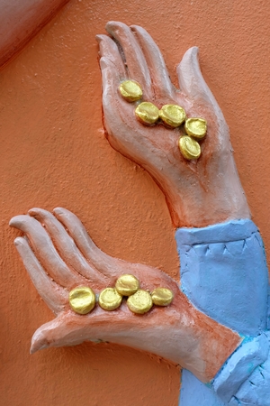 Close up Golden Coins in Sculpture Hand on Concrete Wall.の写真素材