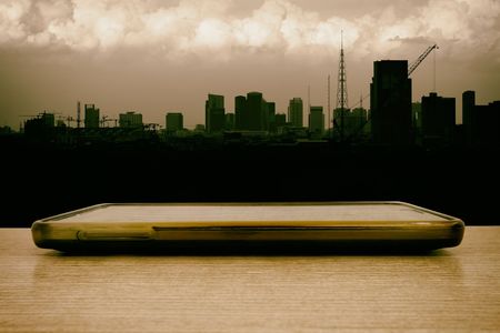 Close-up Beside of Mobile Phone with Silhouette of Cityscape Background.