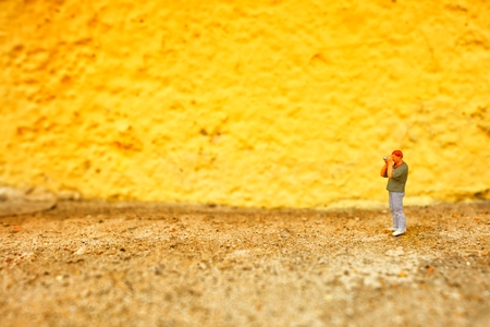 Miniature Figure Photographer with Yellow Painted Concrete Wall Background.