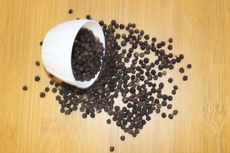 Black pepper in a white bowl on a wooden background. Top view.