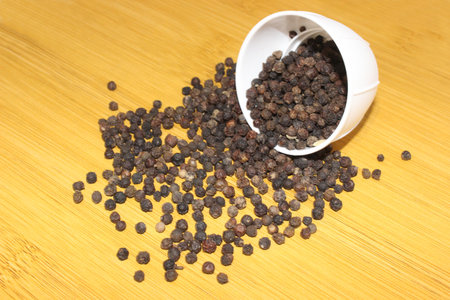 Black pepper in a white bowl on a wooden background. Close-up.