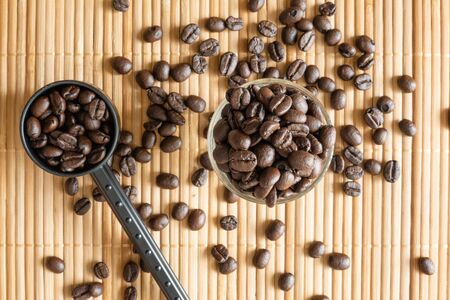 A cup of coffee beans and a measuring spoon on bamboo matの写真素材