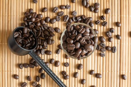 A cup of coffee beans and a measuring spoon on bamboo matの写真素材