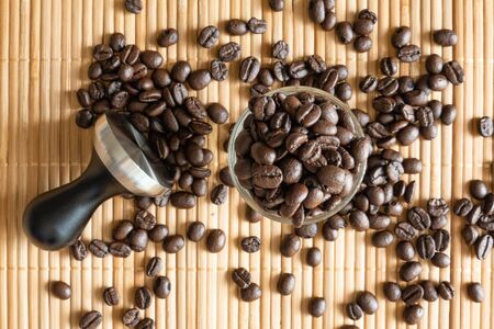 A cup of coffee beans and a tamper on bamboo matの写真素材