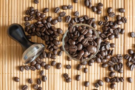 A cup of coffee beans and a tamper on bamboo matの写真素材
