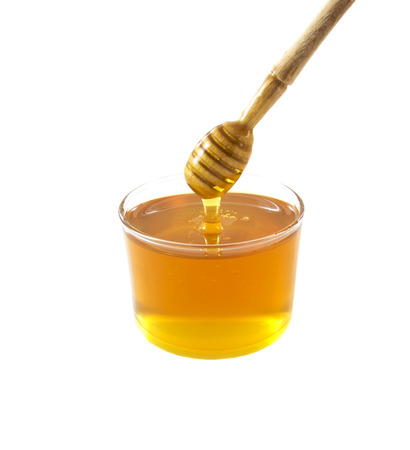 Glass jar of honey with wooden drizzler isolated on white background の写真素材