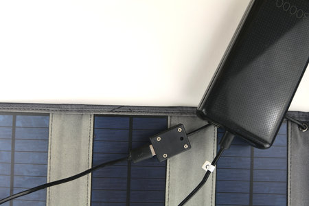 A big black power bank is being charged from a portable solar panel on a white backgroundの写真素材