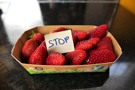 Some delicious, real organic strawberries in a paper container on a black surface with an adhesive note label with the text "stop" on it.の写真素材