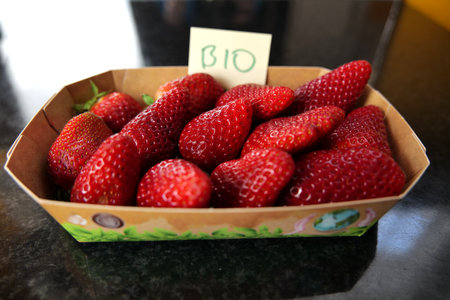Some delicious, real organic strawberries in a paper container on a black surface with an adhesive note label with the text "bio" on it. Bio means it is free of chemicals.の写真素材