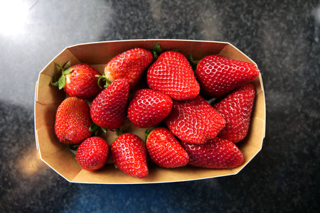 Thirteen pieces of delicious, real organic strawberries in a paper container on a black surface.の写真素材