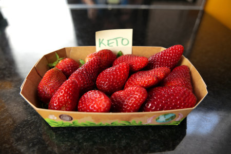 Some delicious, real organic strawberries in a paper container on a black surface with an adhesive note label with the text "keto" on it. The term keto refers to ketogenic diet.の写真素材
