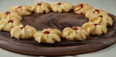 Tea biscuits arranged on a wooden round tray with flour, eggs, vanilla and jam.