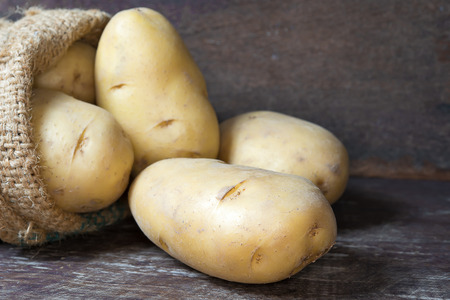 Raw potatoes in burlap bag on  wooden table.の写真素材