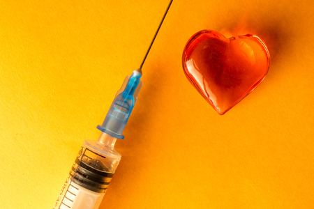 medical syringe and a glass heart lying on green colored paper, heart, loveの写真素材