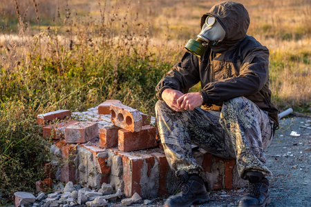 old bricks from destroyed building and man sitting in gas mask on these bricks, fallの写真素材