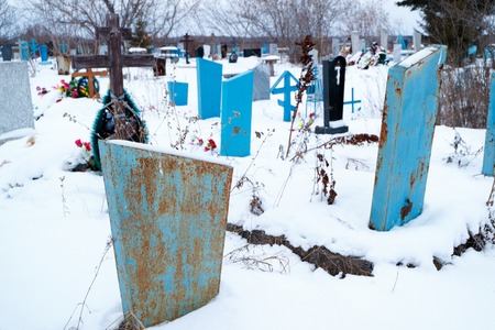 iron gravestones in the cemetery in winter are very noticeable against the background of snow, a cemetery in the countryside in Russiaの写真素材
