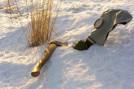 Gas mask and ax in the snow on the field with dry grassの写真素材