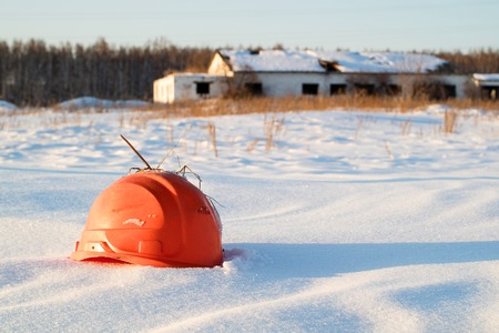 broken orange construction helmet on the background of a ruined building in a snowdrift, waves of snowの写真素材