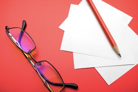 on red background glasses for computer and pencil with leaves