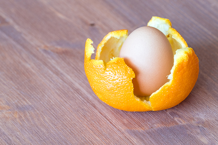 on a brown wooden background an egg in orange skin, orange skin and a heartの写真素材