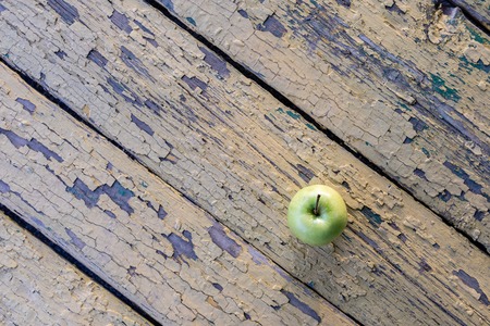 view from above on a green apple located on a background of old boards with peeling yellow paint,...
