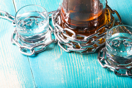 a bottle of rum and two glasses next wrapped with a metal chain, a wooden backgroundの写真素材