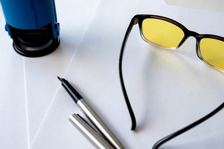 yellow glasses for a computer and a metal pen on a sheet of white paper, an office stamp for...