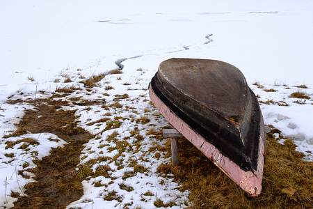 an old wooden homemade boat is kept in winter near a frozen pond, a boat in winterの写真素材