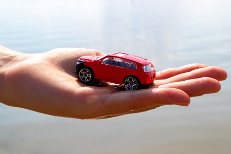 on the children's palm is a red car, the background of the sea warm summer day