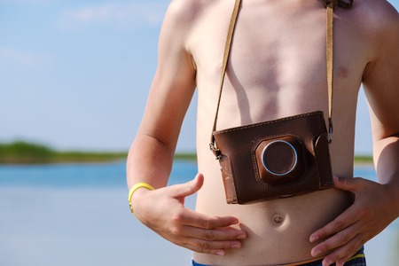 the torso of a young man with a camera on his neck, a camera in a leather cover on the background of...