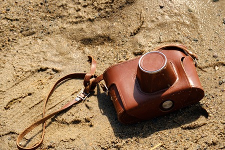 on the wet sand is a camera in a brown leather cover, travel in the summer lost the deviceの写真素材
