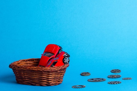 in a wicker basket of twigs are two red cars for children, next to the gears are made of metalの写真素材