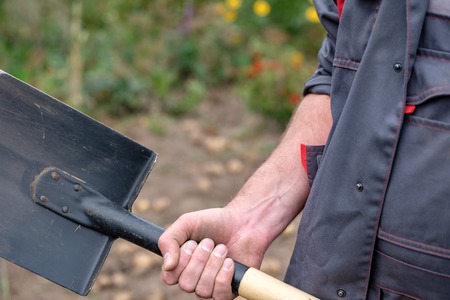 shovel in the hands of a man in overalls gray background outside the gardenの写真素材