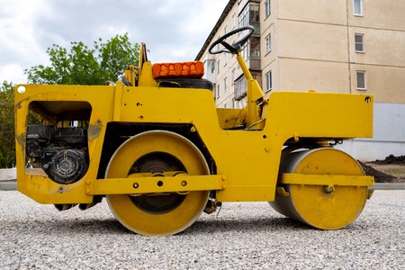 yellow old road roller in the yard of the house make sidewalks, background wood and sky