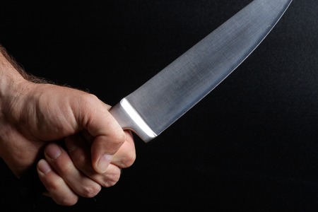 a large kitchen knife in the hand of man, the background is black
