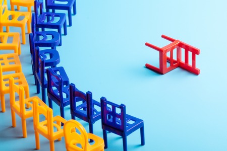 on a blue background, two rows of chairs are set in a semicircle, opposite them is a red chair on...
