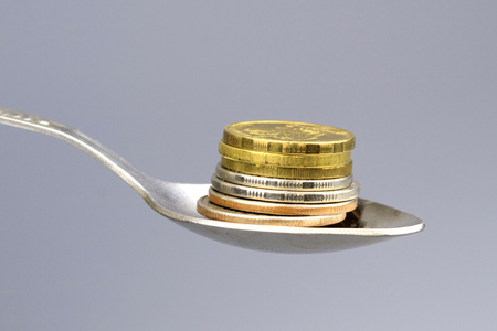the coins are stacked on top of each other with a stack, the coins are in a metal teaspoon, the background is grayの写真素材