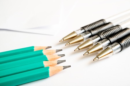 on a white background are simple graphite pencils and pens in front of pencils, paper sheets in the background, the shadow of the sheetsの写真素材