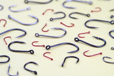different in color and size fishing hooks scattered on the yellow surface, the pattern of the hooks in perspectiveの写真素材