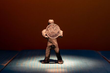 lit from above by a beam of light plasticine man holding a coin ruble