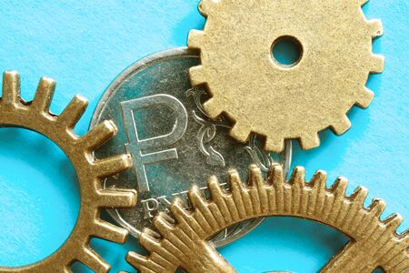 blue background on it metal gears with teeth that touch the old coin on the coin shows the symbol of the Russian rubleの写真素材
