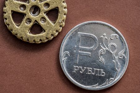 round gear and the round coin with face value of one ruble on brown backgroundの写真素材