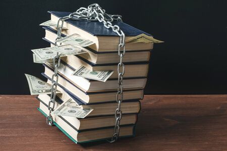 a stack of books tied with a chain of books sticking out money. banned books chained but they have valuable knowledge that can bring profitの写真素材