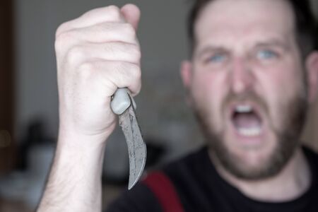 screaming man with a curved knife in his hand in the background out of focus in the foreground knife...