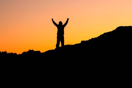 a photograph of a man standing on the mountains holding his hands up against the red skyの写真素材